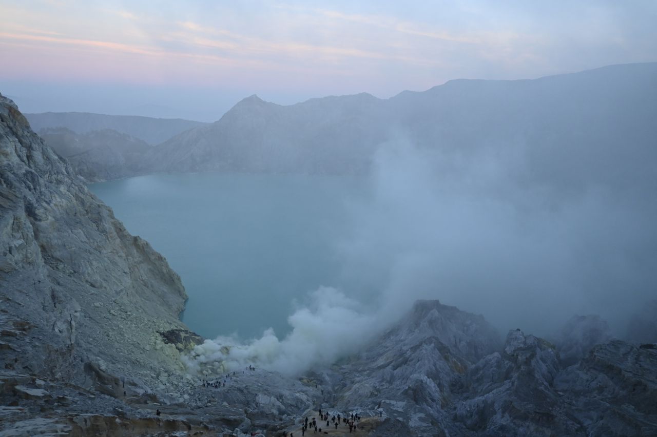 A breathtaking view of Kawah Ijen's turquoise crater lake shrouded in mist at sunrise.