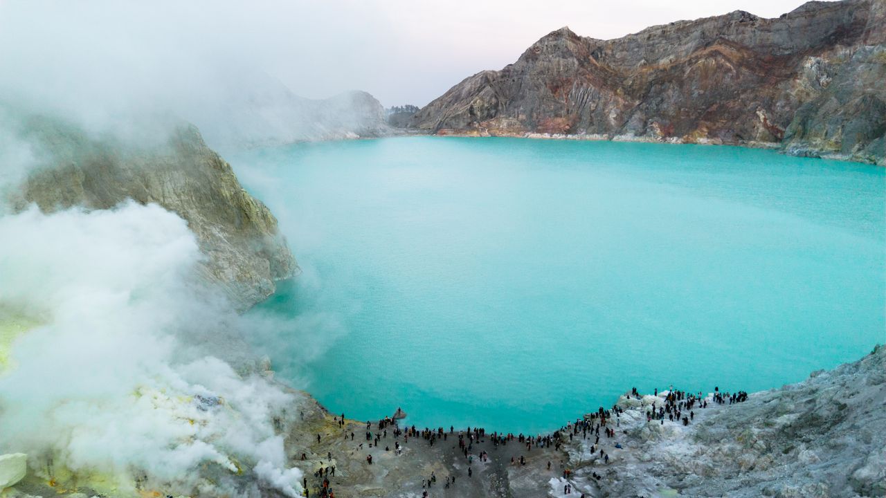 A breathtaking aerial view of Kawah Ijen crater lake with turquoise water and volcanic steam formations.