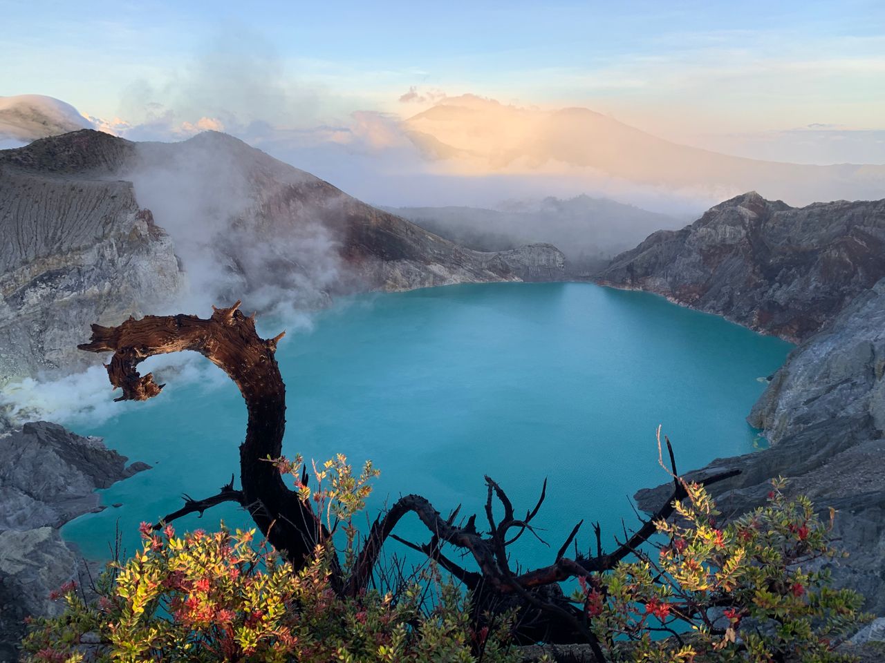Stunning sunrise over Kawah Ijen crater lake with vibrant turquoise water and scenic mountains.